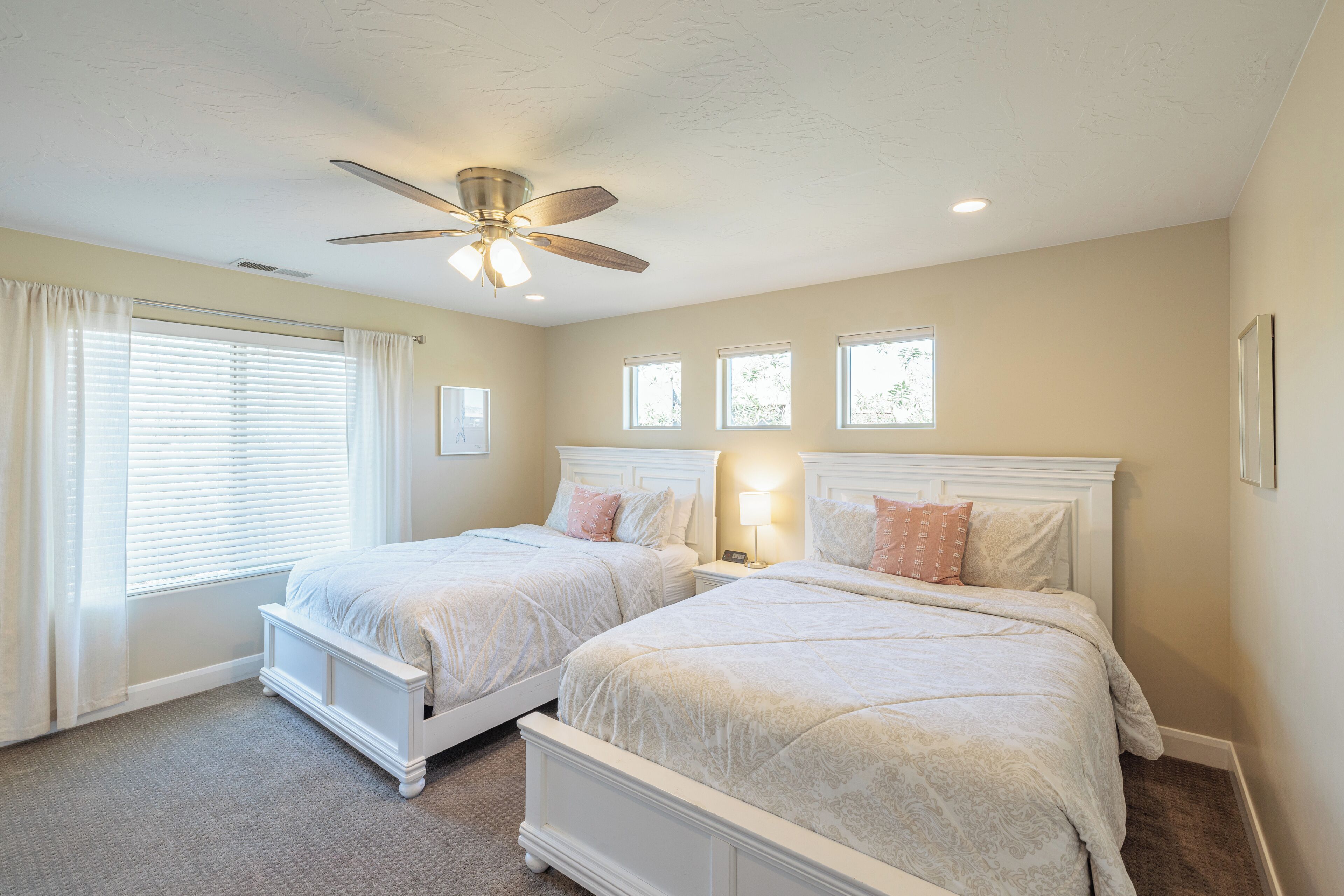 A bedroom with two beds, a ceiling fan, and three windows.