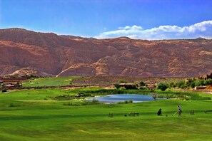 A golf course with a lake, mountains, and a building in the background.