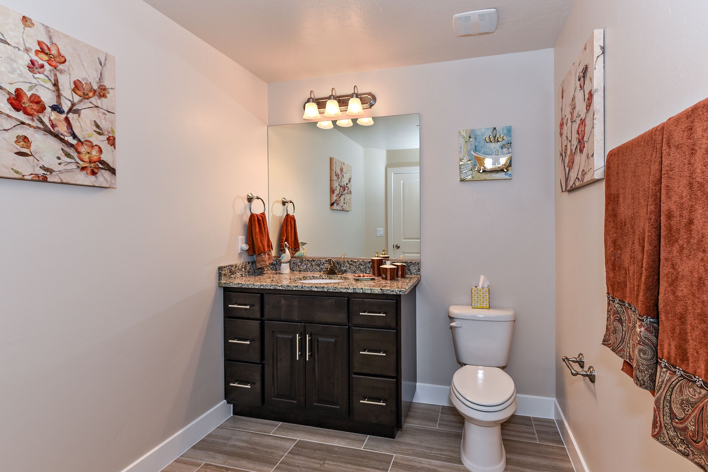 Une salle de bain avec un comptoir en granit, des meubles sombres, des toilettes blanches et un grand miroir.