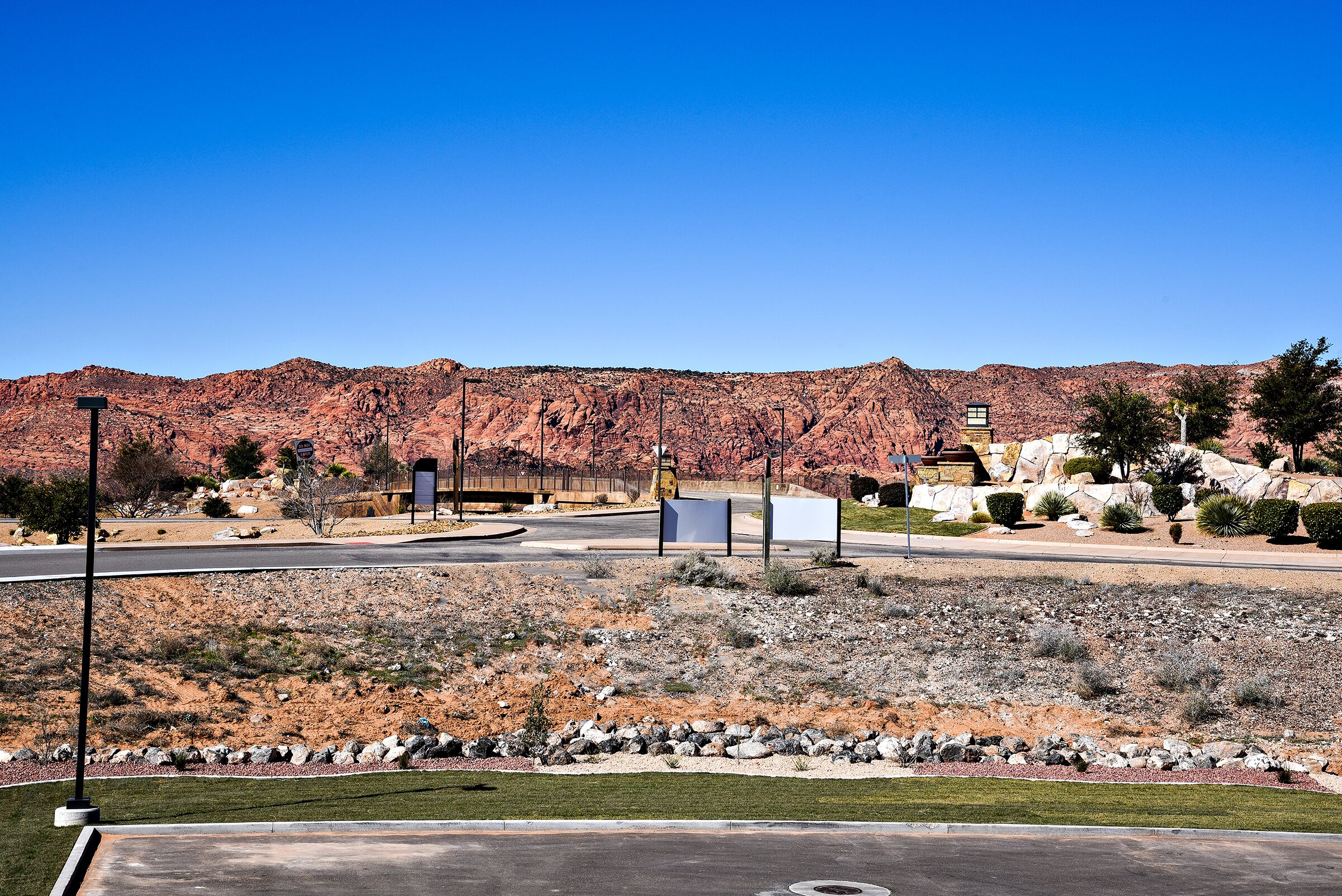 A desert landscape with a paved road, a small building, and a clear blue sky.