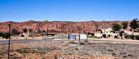 A desert landscape with a paved road, a small building, and a clear blue sky.