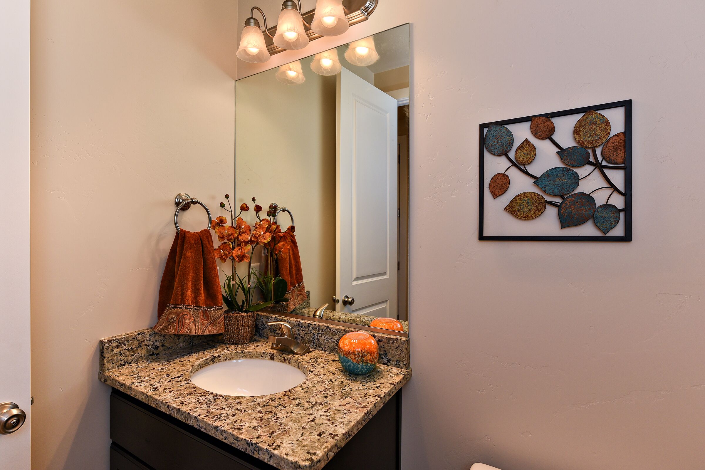 A bathroom with a granite countertop, a sink, a mirror, and a decorative wall piece.