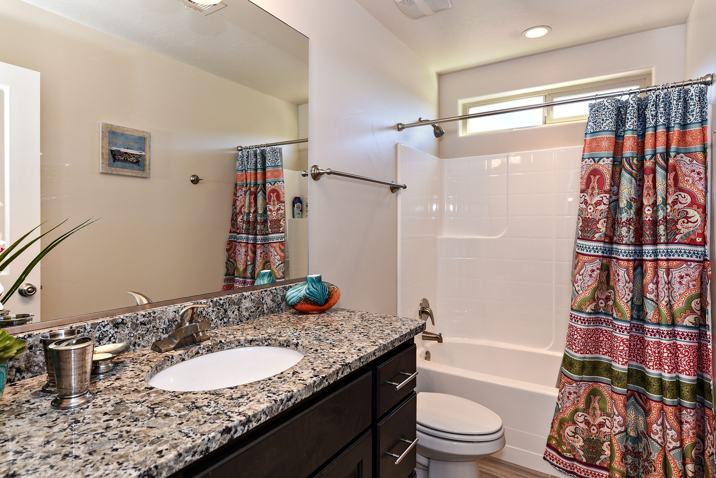 A bathroom with a granite countertop, a white sink, a mirror, a shower curtain with a paisley pattern, and a toilet.