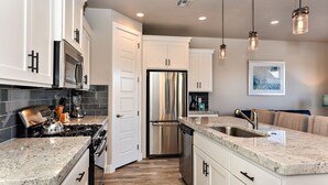 A modern kitchen with white cabinets, stainless steel appliances, granite countertops, and pendant lighting. - Spacious 3BR Sleeps 10 - Poolside on the 9th Hole (St. George)