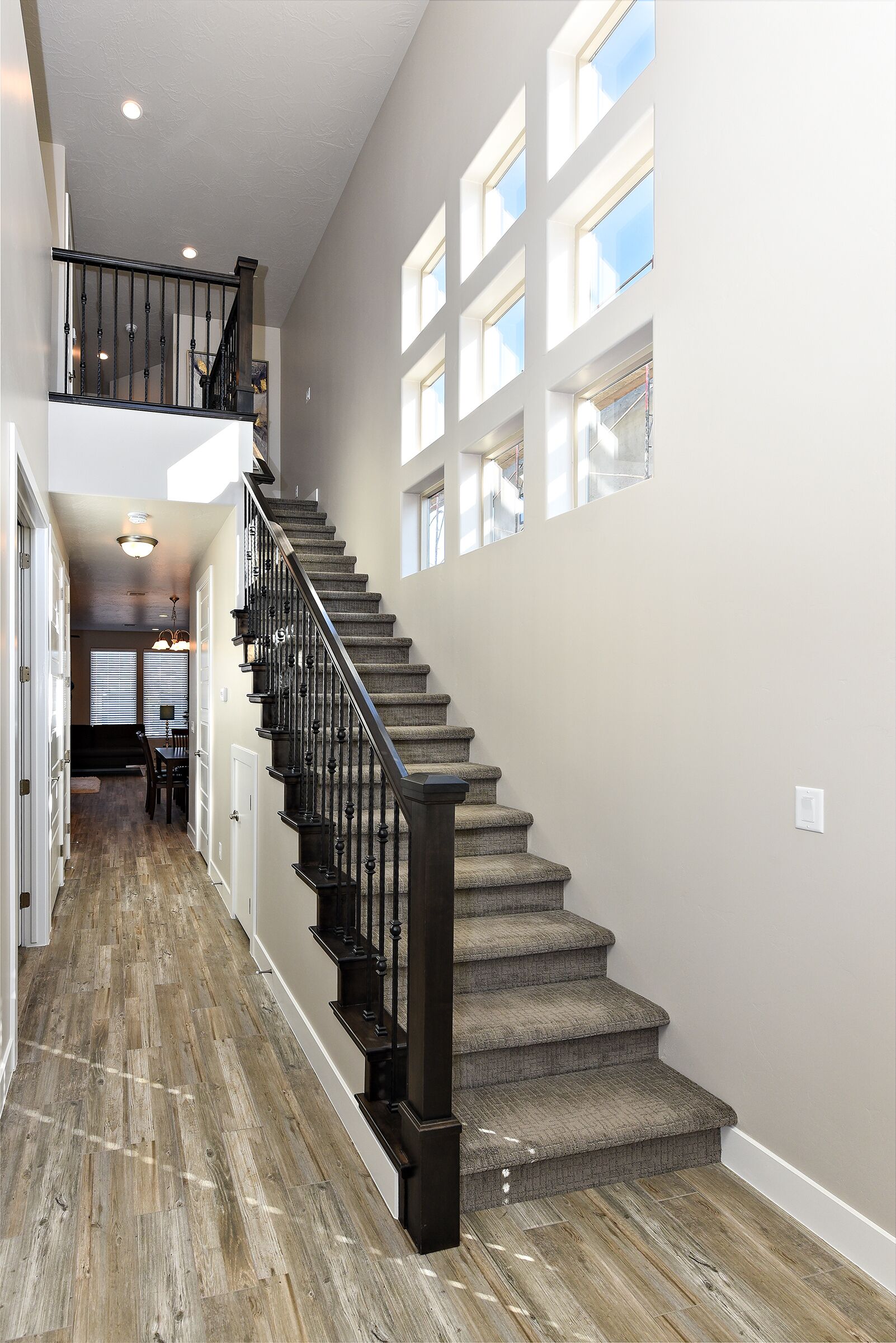 A staircase with a wooden floor leading to a second floor, a dining area with a table and chairs, and a view of the outdoors through large windows.