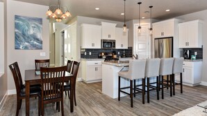 A modern kitchen with white cabinets, a central island, and a dining area with wooden chairs. - Spacious 3BR Sleeps 10 - Poolside on the 9th Hole (St. George)