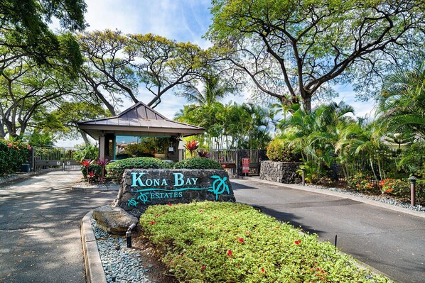 A sign for Kona Bay Estates with a gazebo and tropical landscaping.