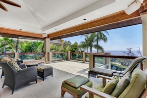 A spacious balcony with wicker furniture, a piano, and a view of the ocean. - 🏖️Great Location | Ocean Front Island Home | Pool | Gated (Kailua Kona)