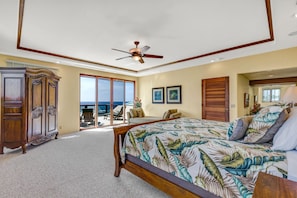 A bedroom with a large bed, a ceiling fan, a view of the ocean, and a sliding glass door leading to a balcony.