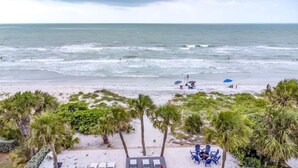 Vista de playa con palmeras, una zona arenosa con sombrillas y algunas personas.