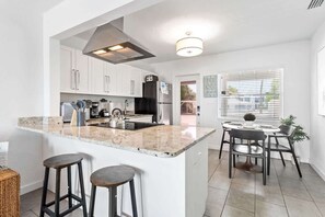 A modern kitchen with white cabinets, a granite countertop, a stainless steel range hood, and a dining area with a round table and chairs.