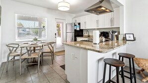 Una cocina moderna con armarios blancos, encimera de granito y una isla integrada con taburetes.