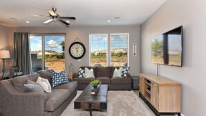 A living room with two sofas, a coffee table, a TV, and a large window with a view of a desert landscape.