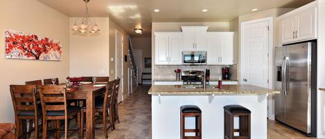 A spacious kitchen with white cabinets, a stainless steel refrigerator, and a dining area with wooden chairs and a table.