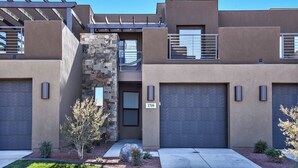 Une maison moderne à deux étages, dotée d’une façade en pierre, de deux portes de garage et d’un petit jardin aménagé à l’avant.