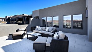 A modern outdoor patio with wicker furniture, large windows, and a view of the desert landscape. - Spacious 4BR on the 9th - Overlooks Pool & Courts (St. George)