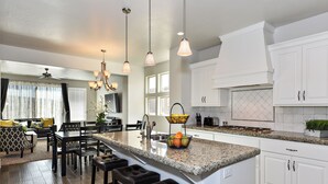 A modern kitchen with white cabinetry, a granite countertop, and a central island with bar stools. - Spacious 4BR on the 9th - Overlooks Pool & Courts (St. George)