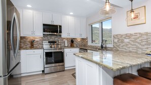 A modern kitchen with white cabinetry, stainless steel appliances, a large island with bar stools, and a view of the outdoors through a window. - Gorgeous Views of Vail and Beaver Creek A702 (Avon)