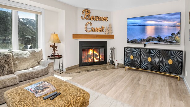 A living room with a fireplace, a sofa, a coffee table, a TV, and a painting of a landscape. - Gorgeous Views of Vail and Beaver Creek A702 (Avon)