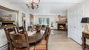 A dining room with a large wooden table, chairs, a chandelier, a fireplace, and a door. - Gorgeous Views of Vail and Beaver Creek A702 (Avon)