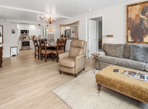 A spacious living room with a sofa, a chair, a coffee table, and a dining area with chairs and a table.