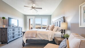 Ein Schlafzimmer mit Bett, Kommode, Fernseher, Deckenventilator und Blick ins Freie.