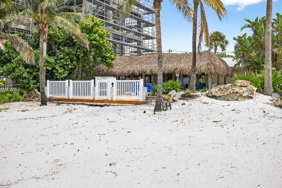 Una propiedad frente a la playa con una estructura de techo de paja, palmeras y una playa de arena.