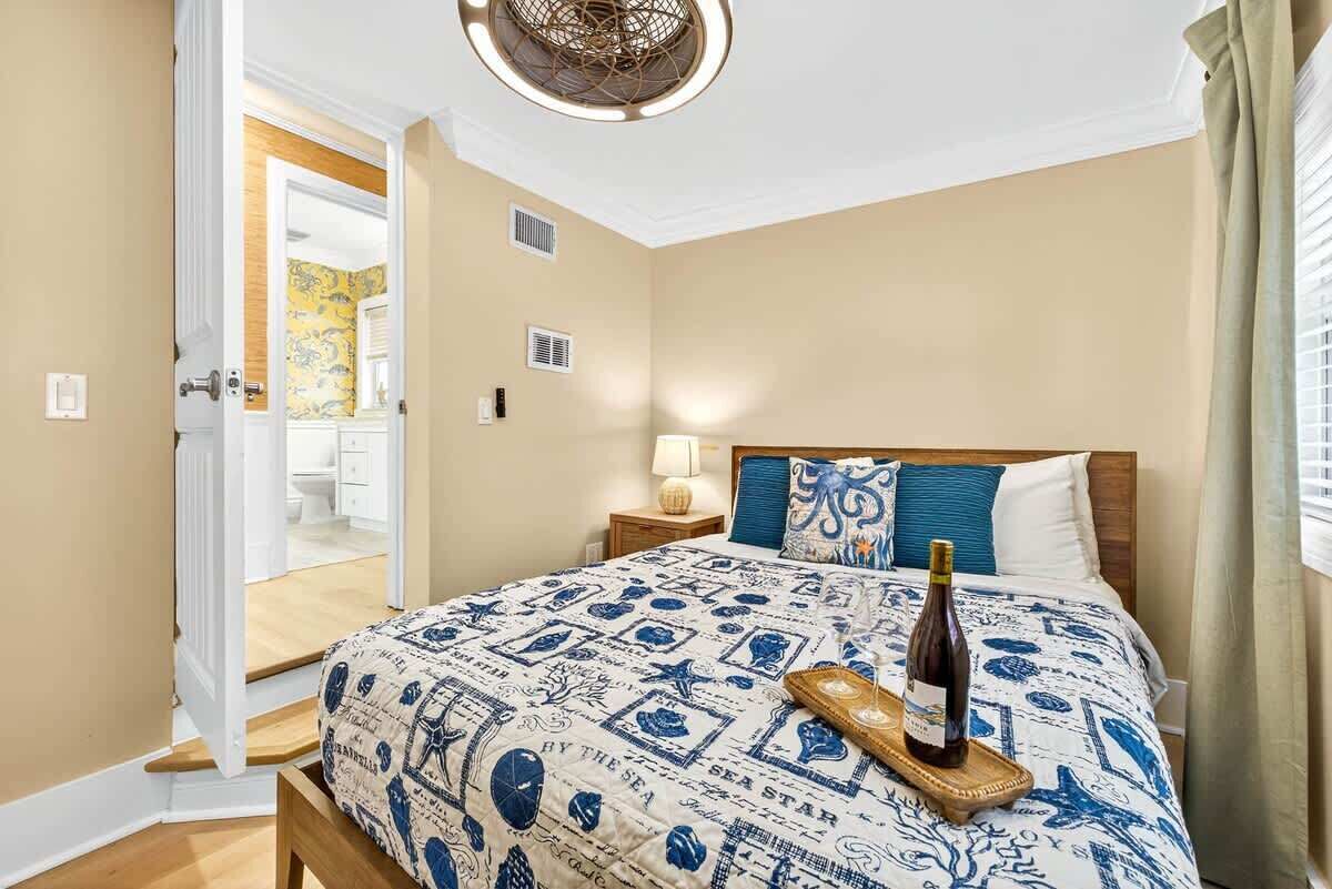Une chambre à coucher comprenant un lit, une table de chevet, une lampe et une porte donnant sur une salle de bain.