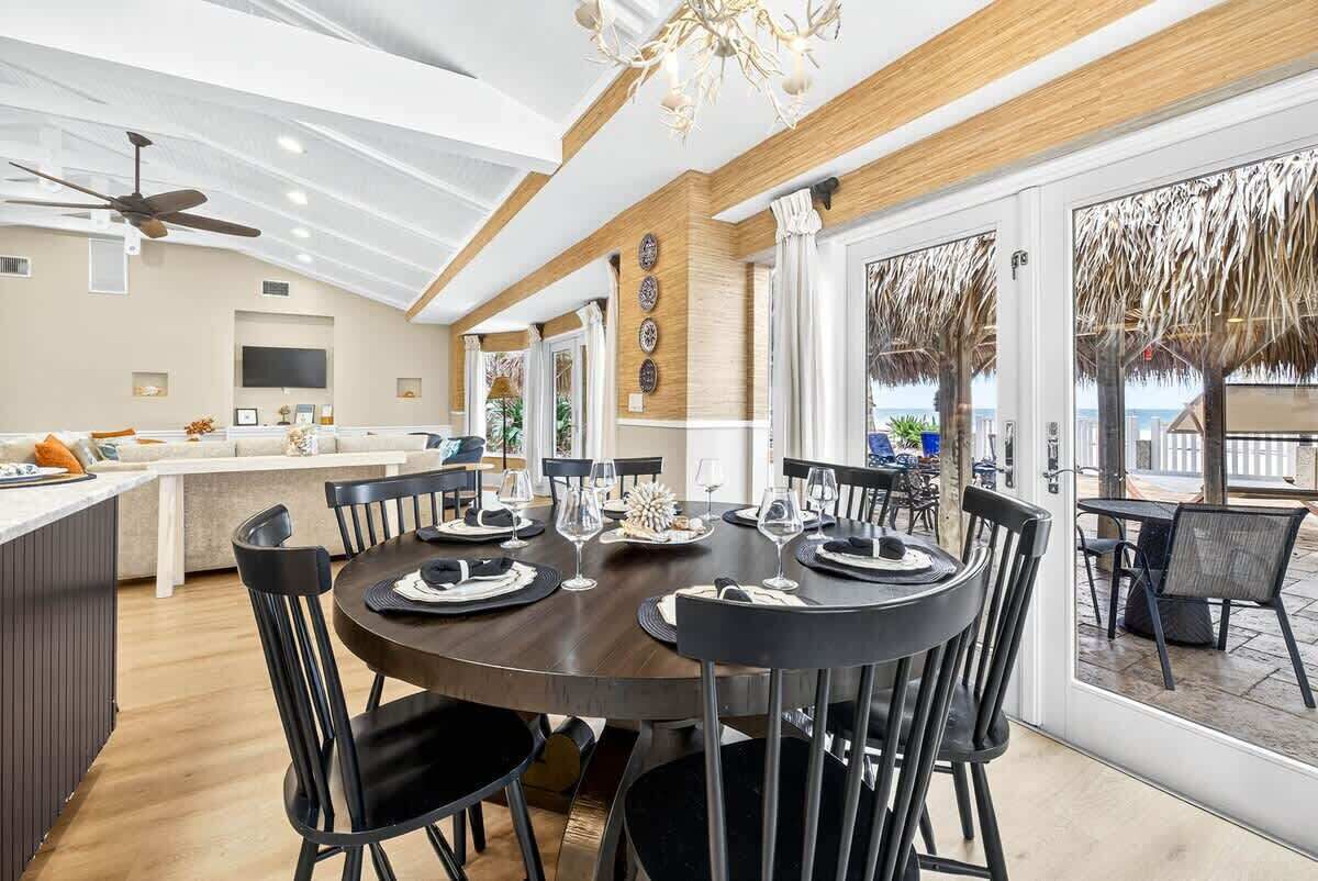 A modern dining area with a round table, black chairs, and a view of the ocean through large windows.