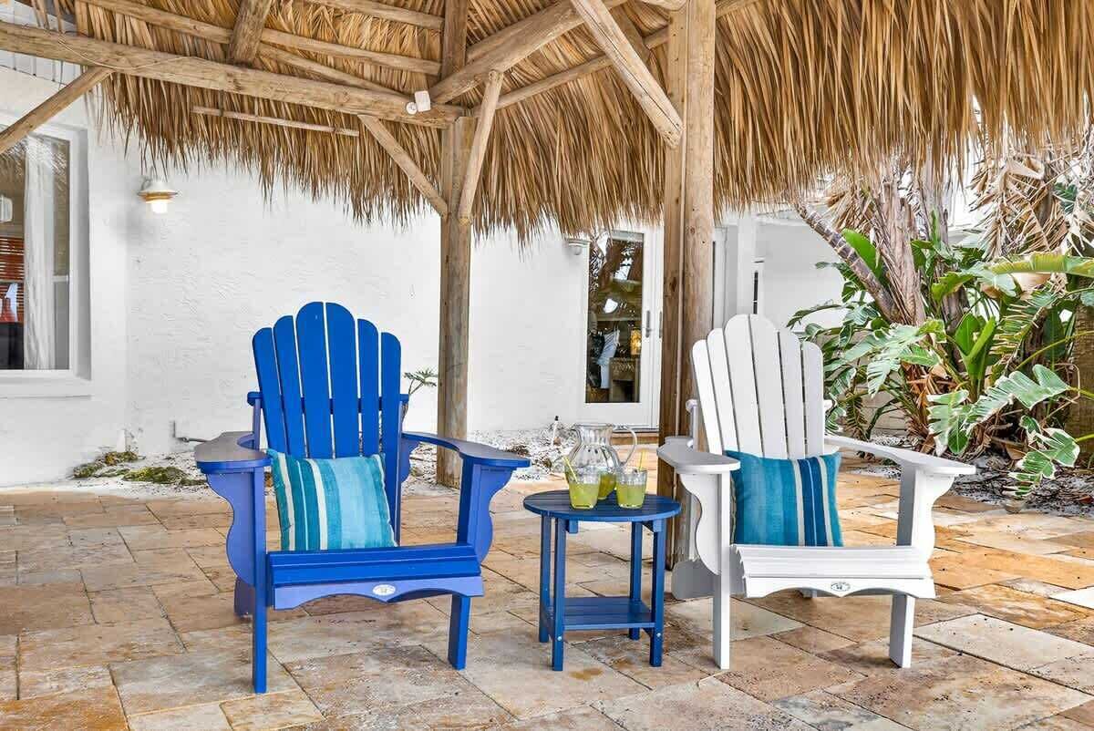 Two chairs with cushions, a small table with drinks, and a thatched roof structure.