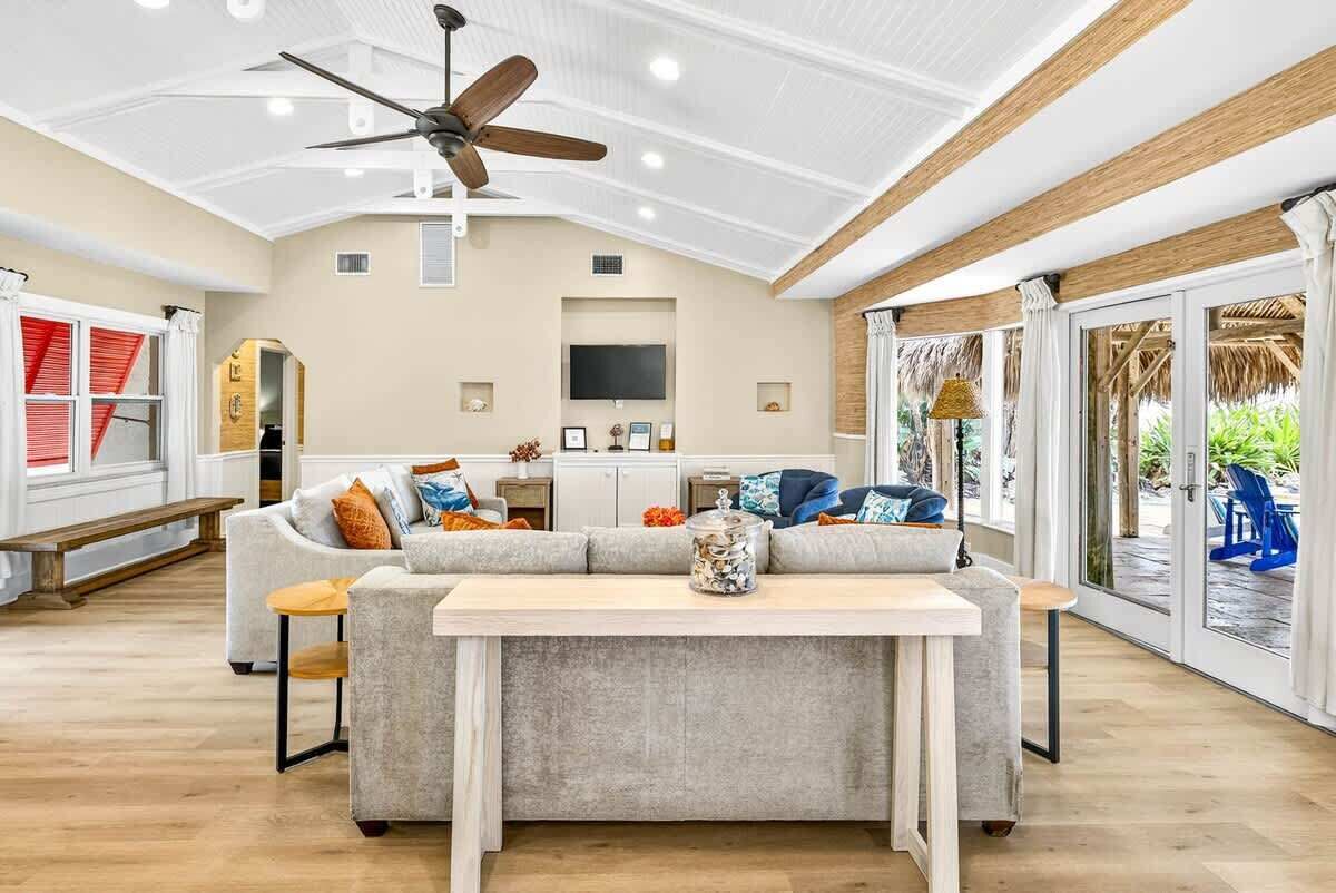 A spacious living area with a ceiling fan, a sofa set, a dining table, and a TV mounted on the wall.