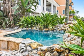 Una piscina circondata da rocce e piante tropicali, con un edificio bianco sullo sfondo.