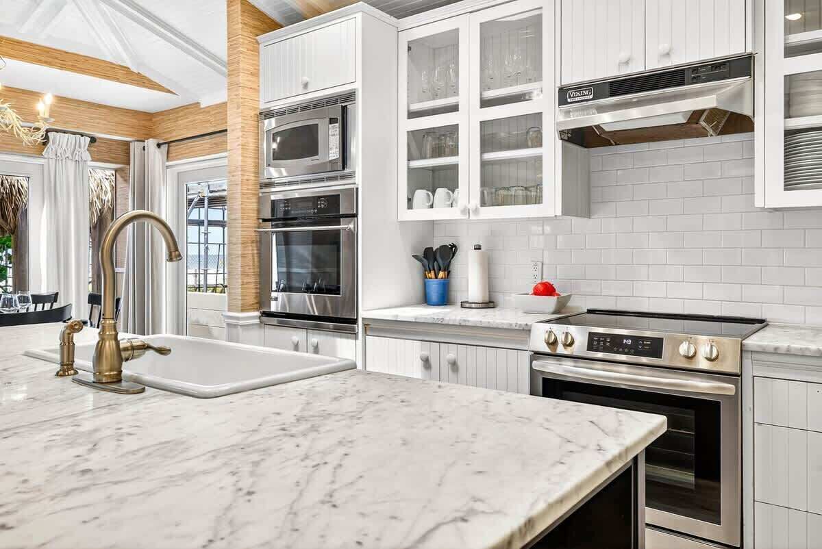 Una cocina moderna con armarios blancos, encimera de mármol, electrodomésticos de acero inoxidable y horno empotrado.