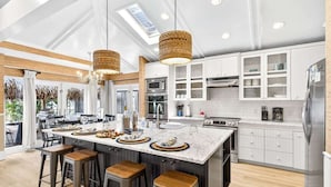A modern kitchen with a large island, bar stools, and a dining area with a view. - Gulf Front Dreams Beachfront Home in Clearwater (Clearwater Beach)