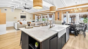 A spacious kitchen with a large island, modern pendant lights, and a dining area with a black table and chairs. - Gulf Front Dreams Beachfront Home in Clearwater (Clearwater Beach)
