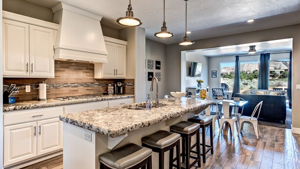A spacious kitchen with a large island, white cabinetry, and a stone backsplash. There are bar stools around the island and a dining area with a view of the outdoors. - Sleeps 17 w/ Pergola Lounge, Fire Pit & Pool View (St. George)
