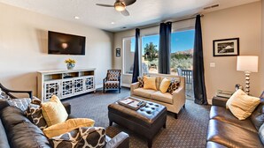 A living room with a sofa, ottoman, and a television. - Sleeps 17 w/ Pergola Lounge, Fire Pit & Pool View (St. George)