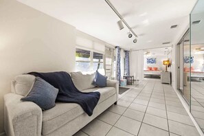 A modern living room with a sofa, a coffee table, and a glass door leading to a kitchen area.