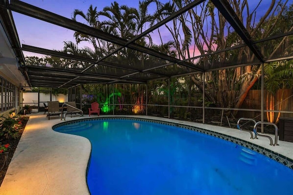 A swimming pool with a curved edge, surrounded by a covered area with chairs and a table.
