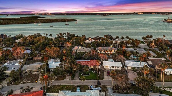 An aerial view of a coastal residential area with houses, palm trees, and a marina with boats.