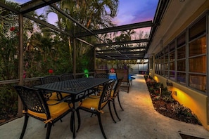 An outdoor patio with a covered seating area, surrounded by lush greenery and palm trees.