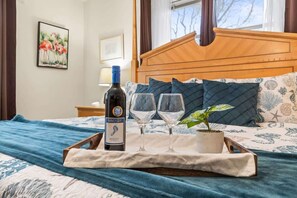 Un lit avec une tête de lit en bois, une bouteille de vin Merlot, deux verres à vin et un plateau avec une plante.