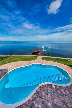 En swimmingpool med udsigt over havet, en træterrasse og en græsplæne.