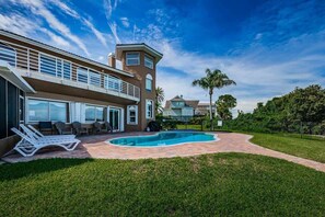Una casa de dos pisos con piscina, mobiliario exterior y un césped bien cuidado.