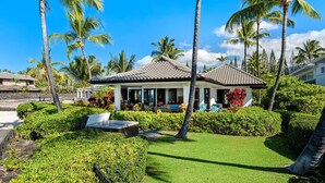 A resort with a covered outdoor seating area, lush greenery, and palm trees.