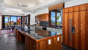 A modern kitchen with a large island, wooden cabinets, and a view of the ocean.