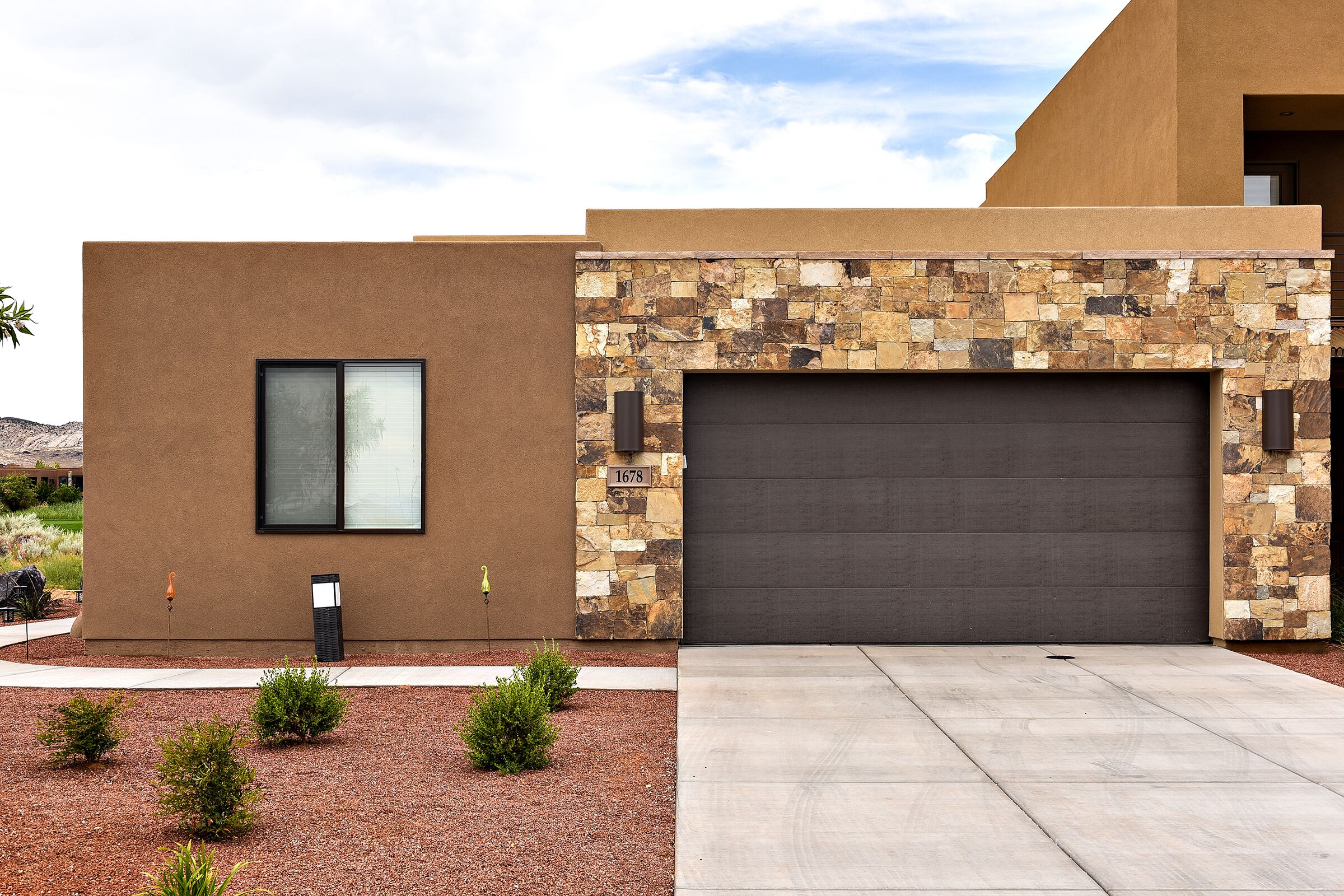 A modern house with a stone facade, a garage, and a small garden with shrubs.