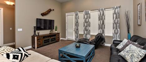 A living room with a sofa, a coffee table, a TV, and a window with curtains.