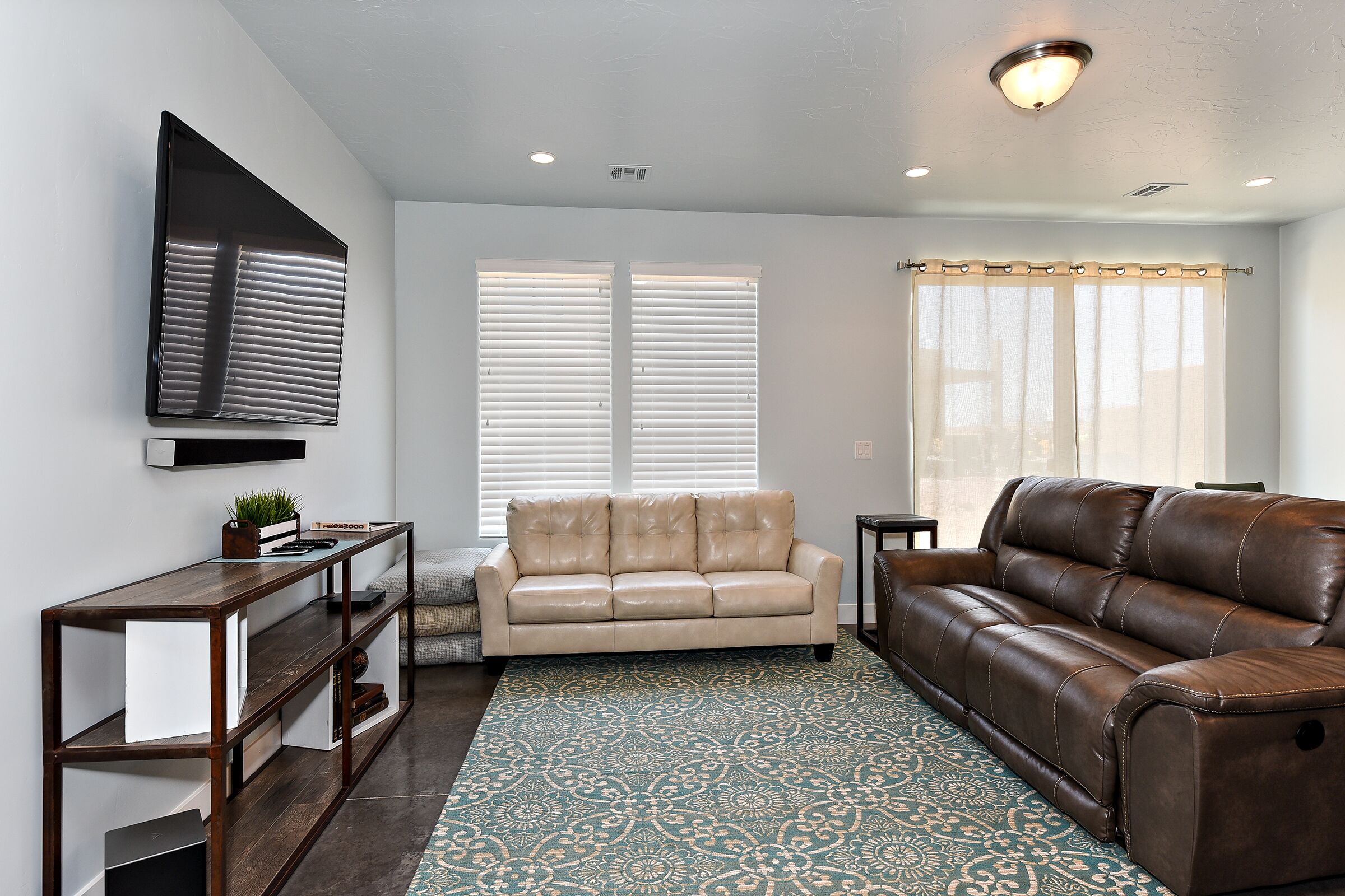 A living room with a beige sofa, a brown leather sofa, a wooden coffee table, and a patterned rug.