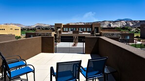 A balcony with blue chairs and a table, overlooking a mountainous landscape and a building with a modern design. - Stylish 4BR on the 18th - Rooftop Deck, Near Pool (St. George)